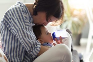Pretty young mother feeding her baby with milk on feeding bottle in the living room of home.