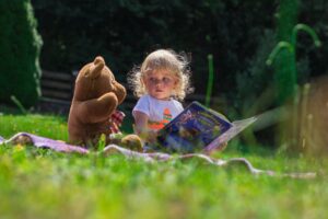 child sitting with book and bear in the summer