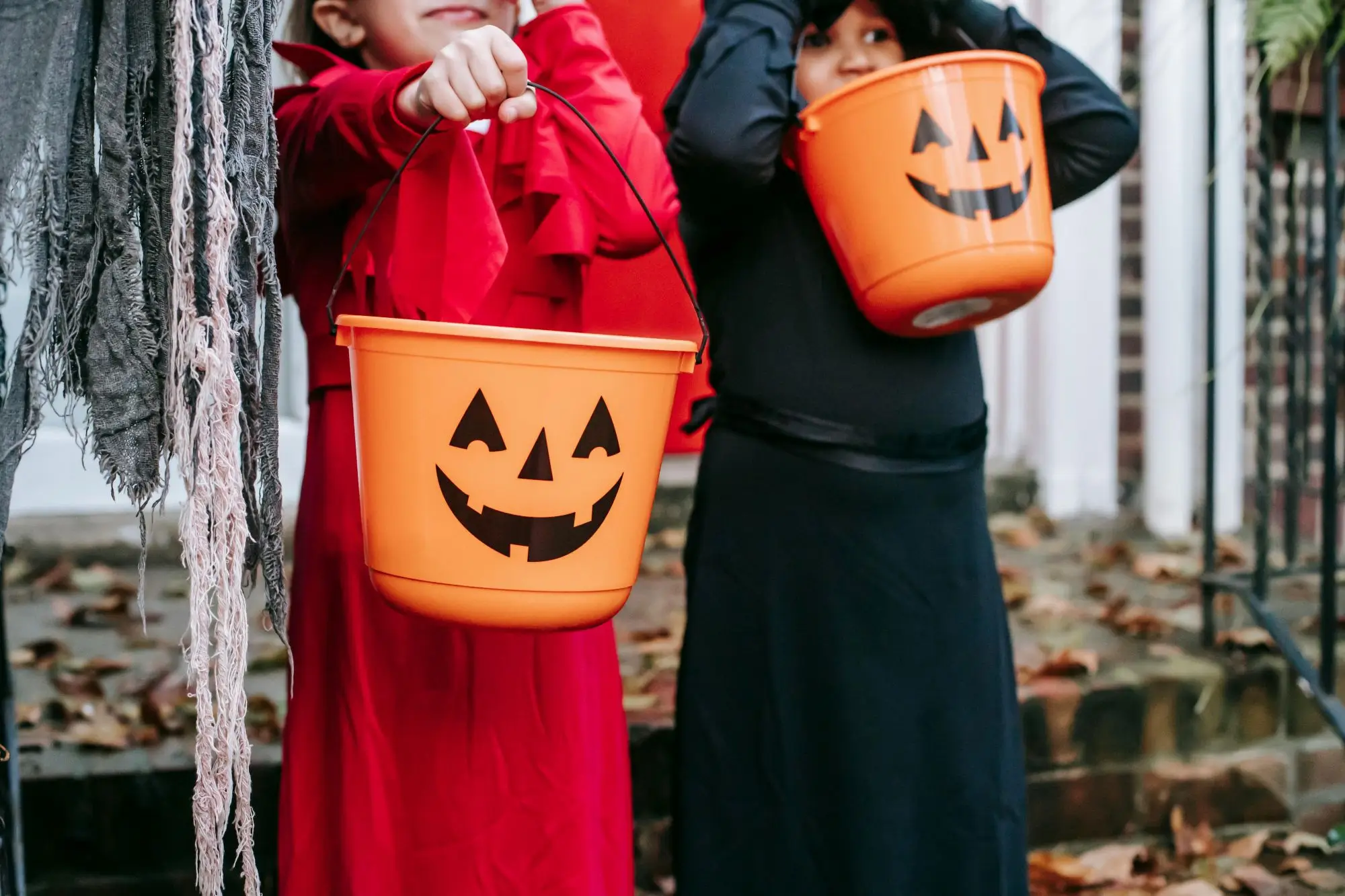 Two kids dressed in halloween costumes holding trick or trick buckets that look like jack o' lanterns